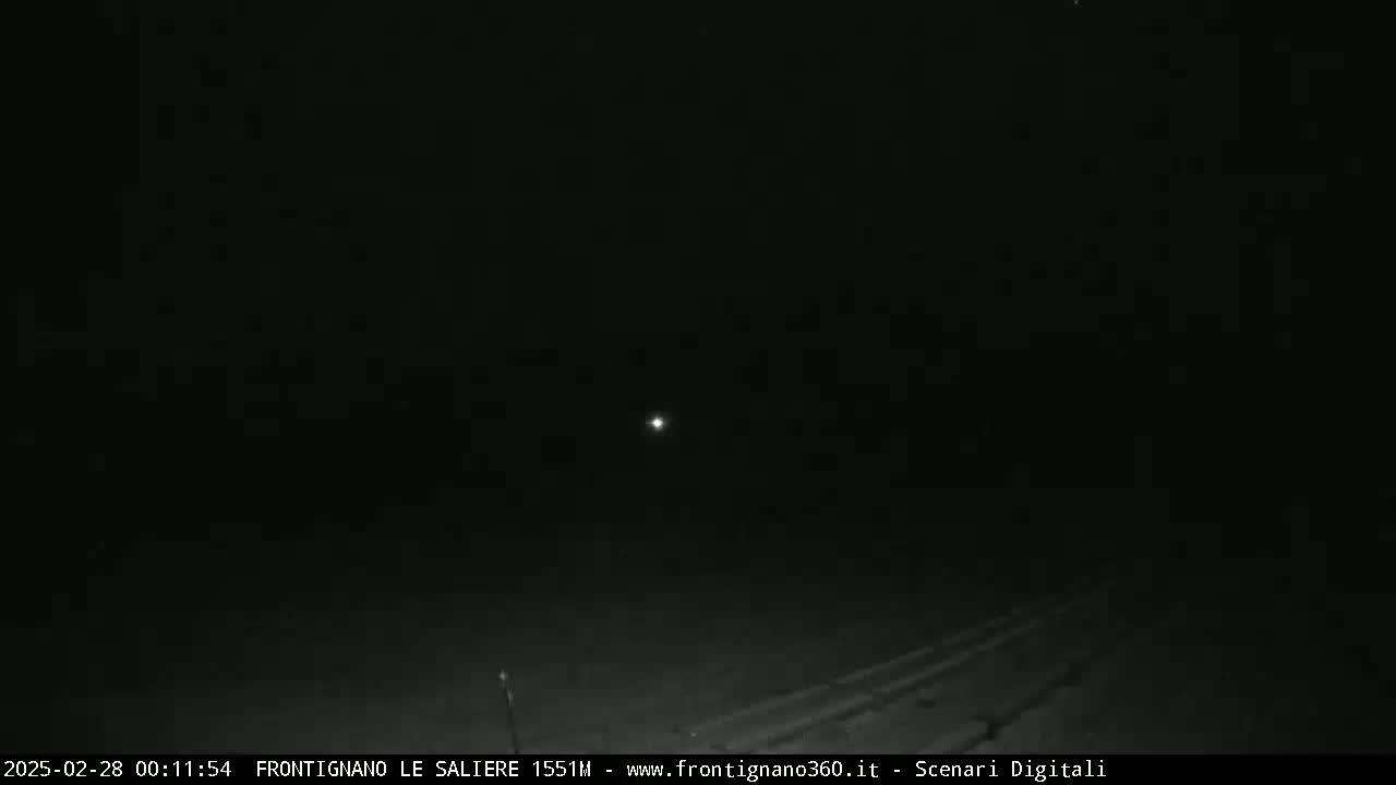 A nighttime, low-light image shows a dark road and a single bright light in the distance.