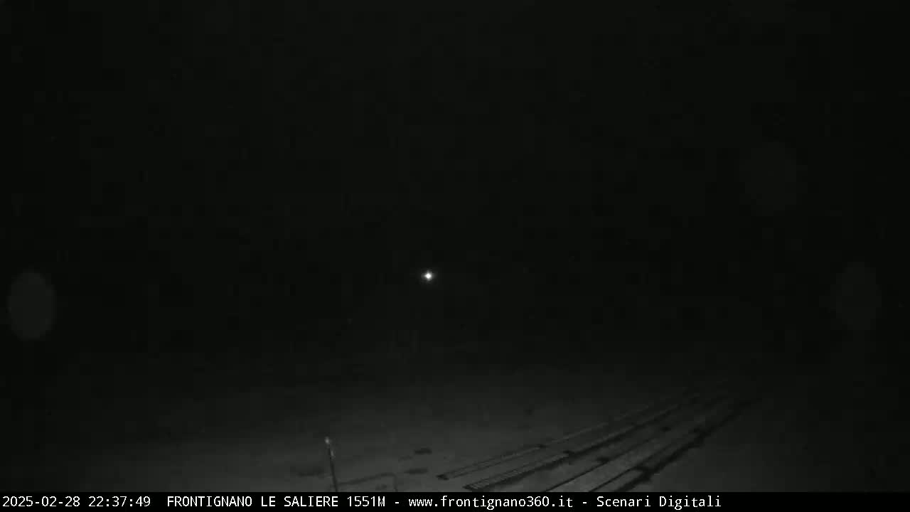 A dark, nighttime scene shows a single, distant light source in the center of the frame, with faint horizontal lines in the bottom portion.