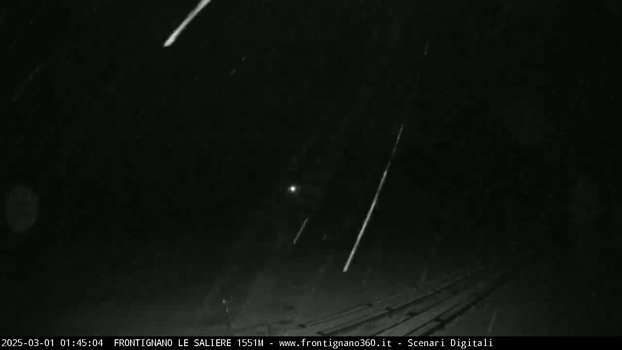 Multiple meteors streak across a dark, nighttime sky that is also experiencing light rain or snow.