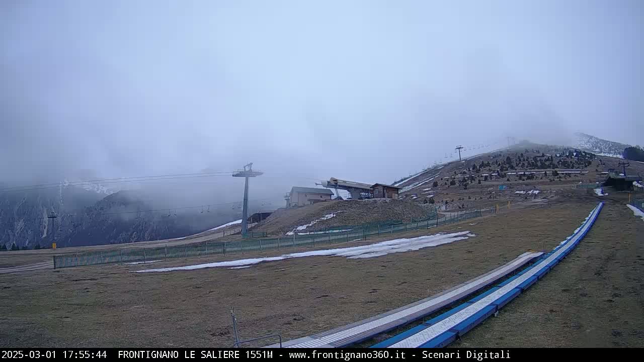 A foggy mountain ski resort with chairlifts, ski runs, and a few buildings is shown.