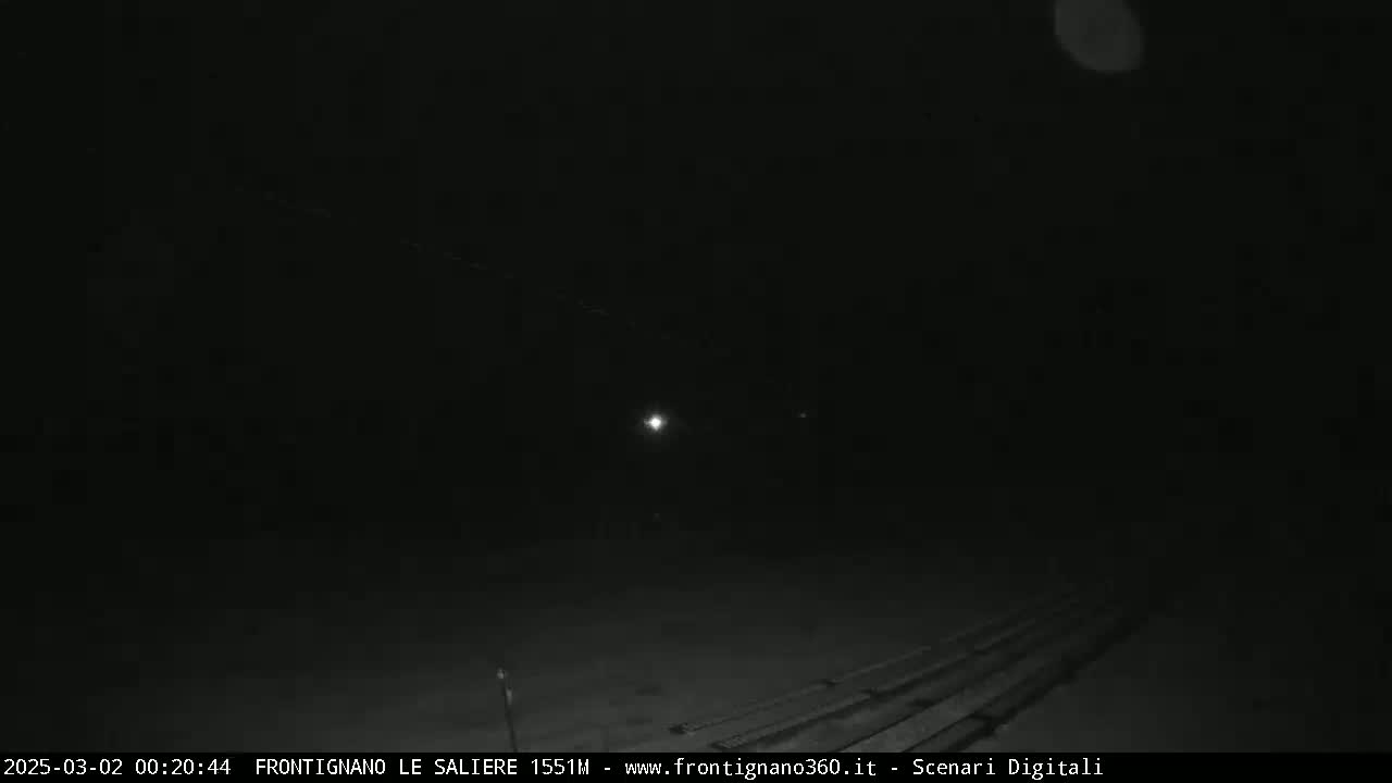 A nighttime view of a dark, possibly paved, surface with faint lights in the distance under a mostly clear sky.