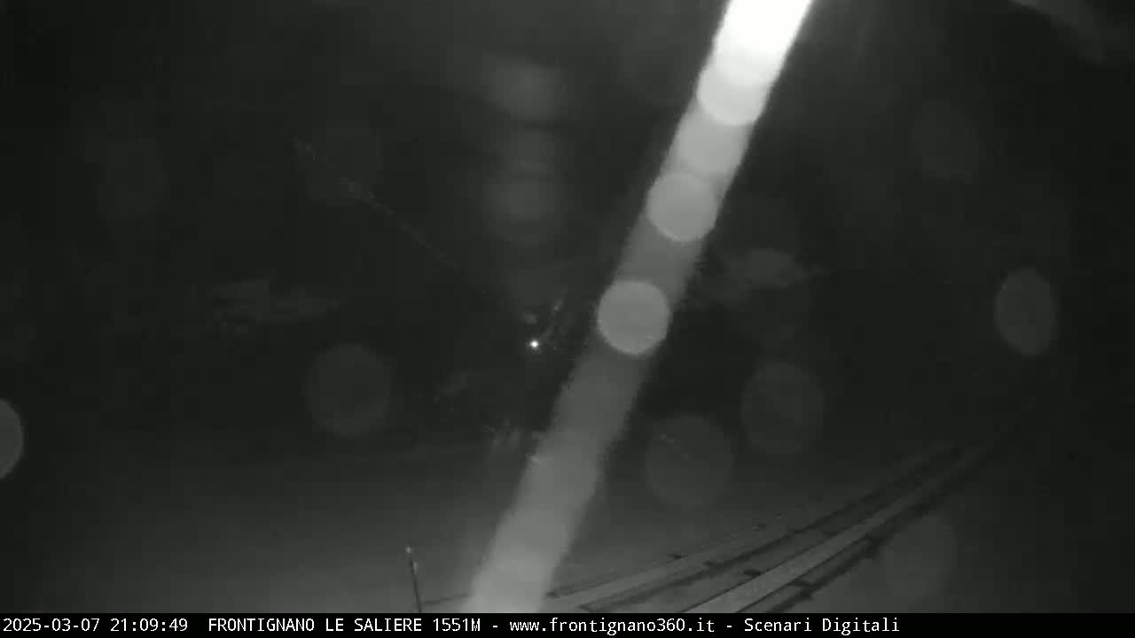 A blurry, nighttime image shows indistinct shapes and bright lights in what appears to be a dark outdoor area with some kind of structure or objects on the ground.