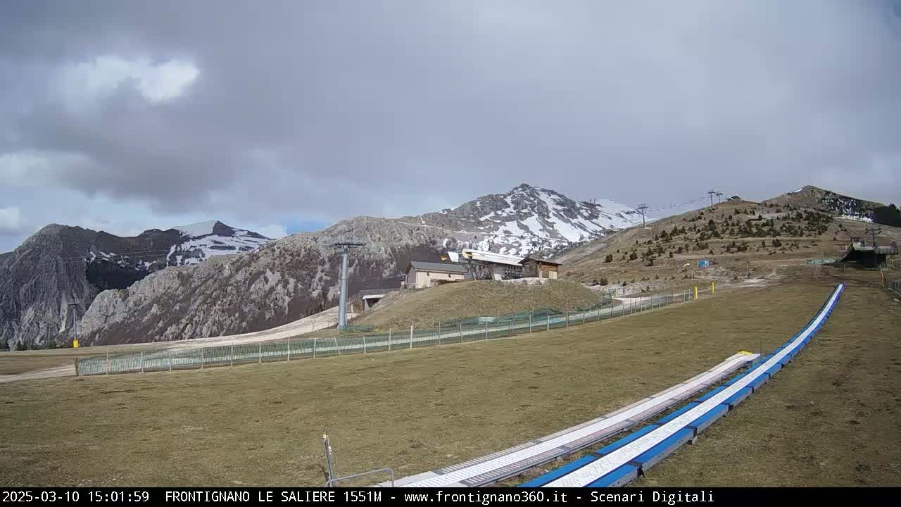 A ski slope with snow-capped mountains in the background under an overcast sky.