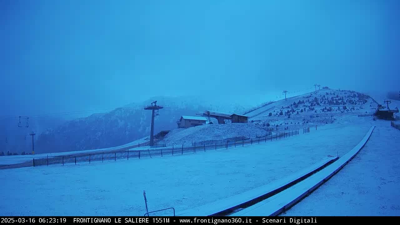 A snow-covered ski slope with ski lifts and a small building is visible under an overcast blue sky.