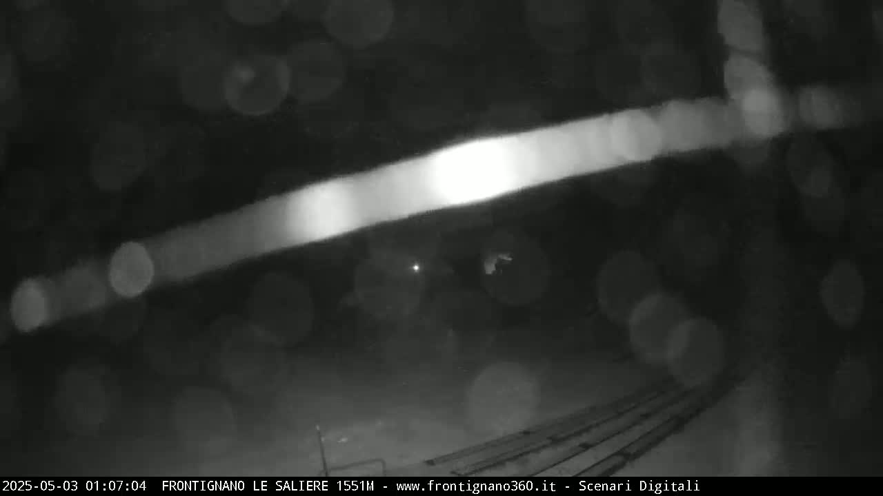 A blurry nighttime image shows a bright streak of light across a dark, possibly rainy, outdoor scene.