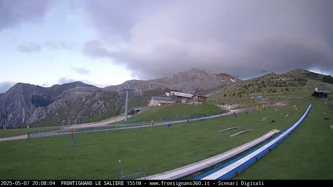 A grassy mountainside with a ski lift and a pair of long, blue ramps under an overcast sky.