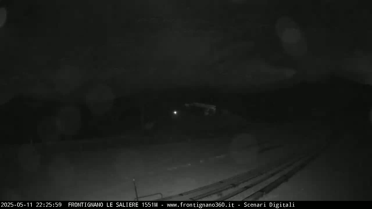 A nighttime, low-light view shows a dark, possibly snowy or overcast scene with faint light sources in the distance.