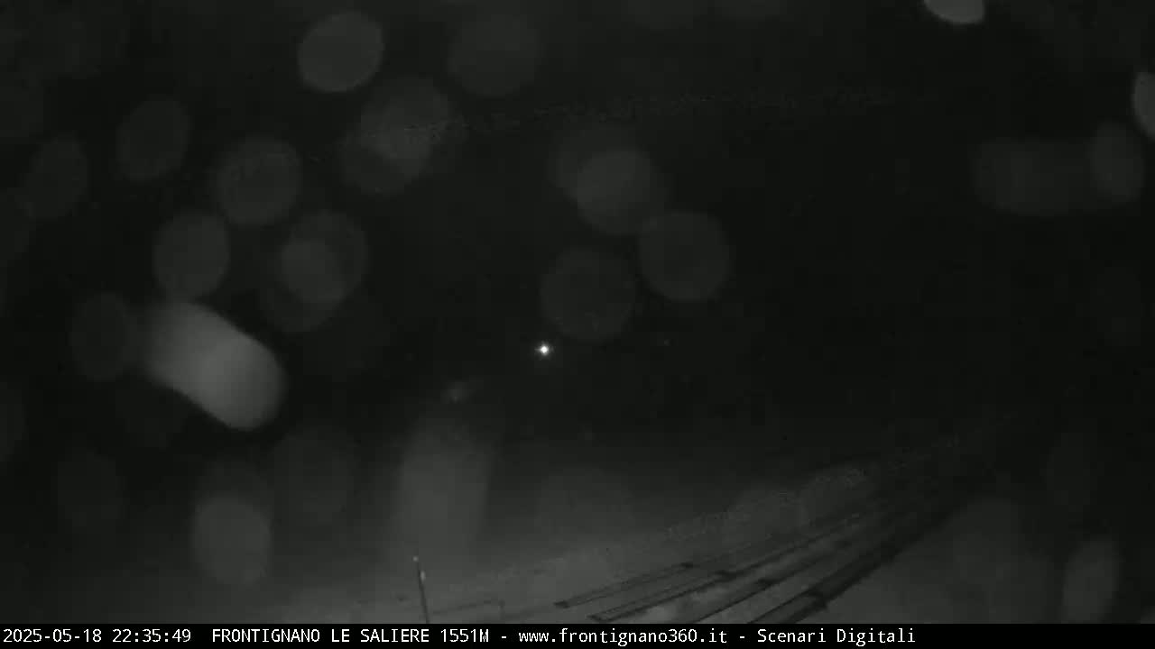 A nighttime, snowy scene shows blurred lights and a dark, snow-covered ground with faint train tracks.