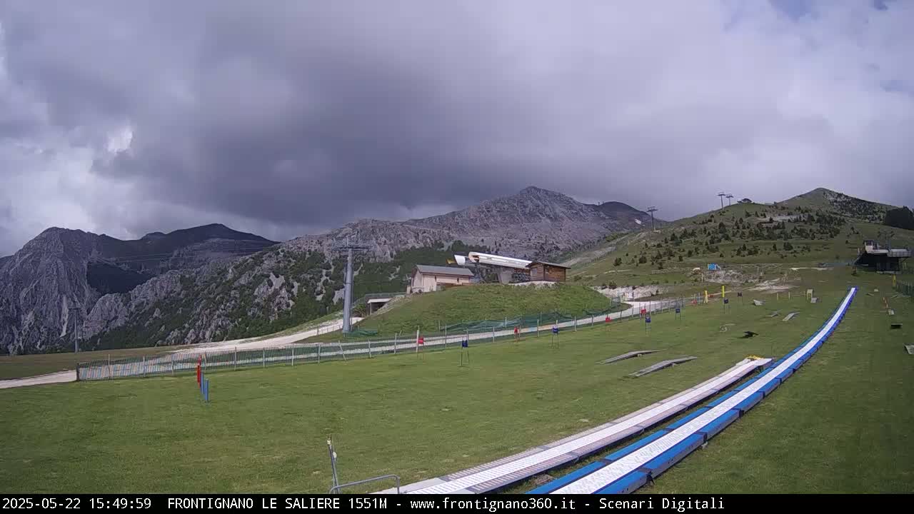A grassy mountaintop area with a ski lift and two long, flat ramps under an overcast sky.