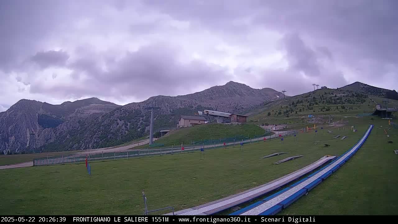 A grassy mountain area with a ski lift and what appears to be a summer luge run under an overcast sky.
