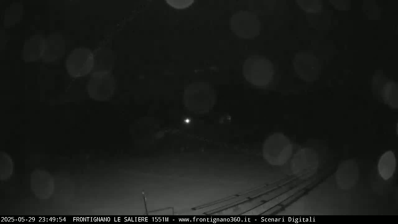 A nighttime outdoor scene shows a dark, possibly snowy or rainy, area with blurry lights in the distance.