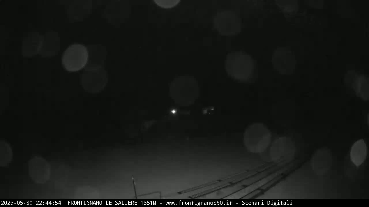 A nighttime, snowy scene shows blurred lights and a dark, possibly snow-covered ground with parallel lines in the bottom right.