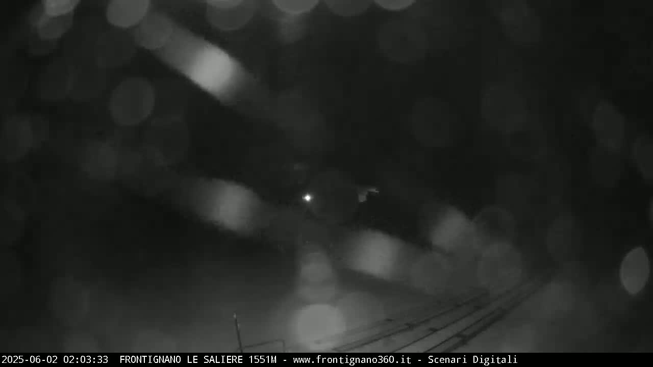A blurry, nighttime image shows a dark, rainy scene with faint lights in the distance.