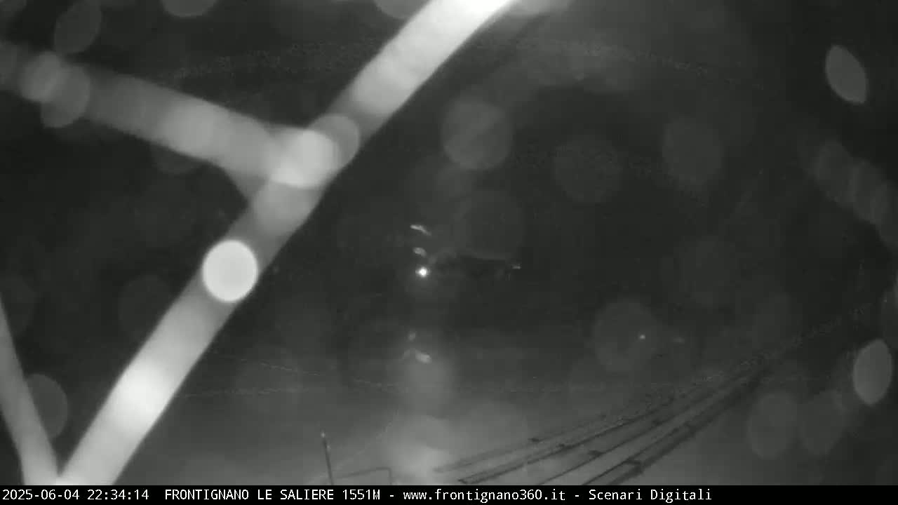 A blurry nighttime image shows a vehicle driving on a snow-covered road with blurred lights in the foreground.