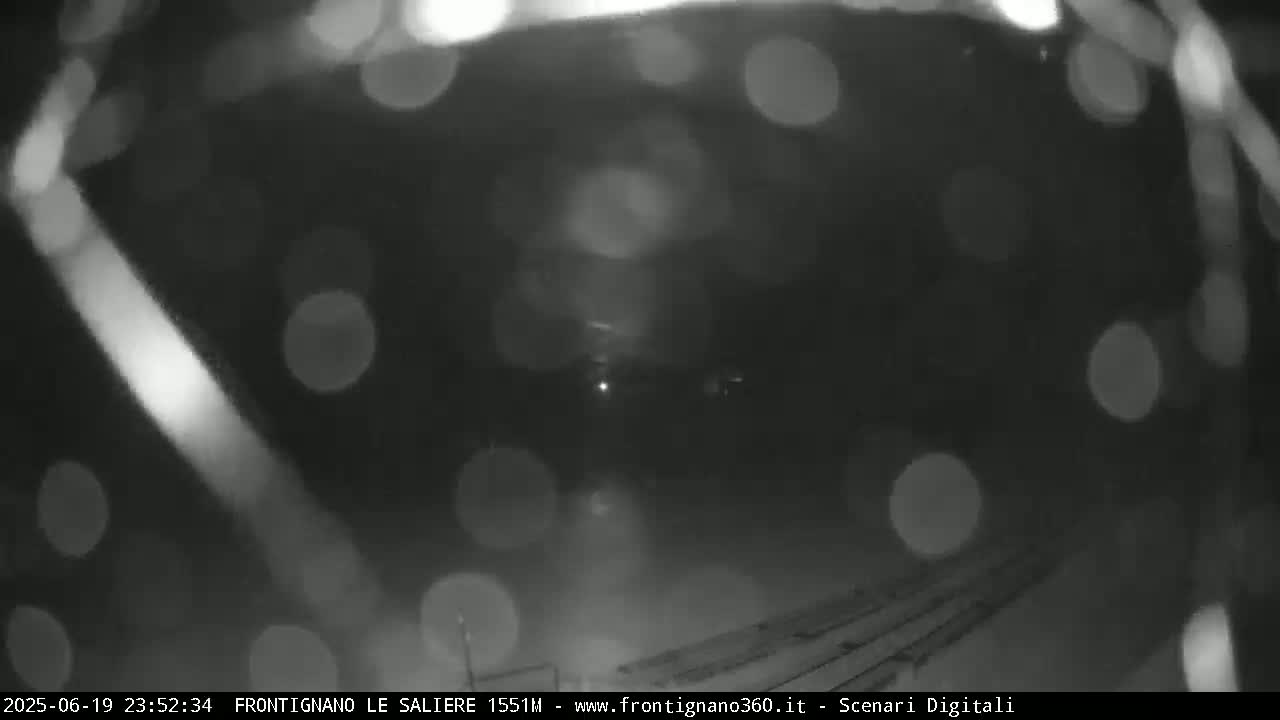 A blurry nighttime image shows a dark scene with indistinct shapes and bright, out-of-focus spots of light, possibly from rain or snow.