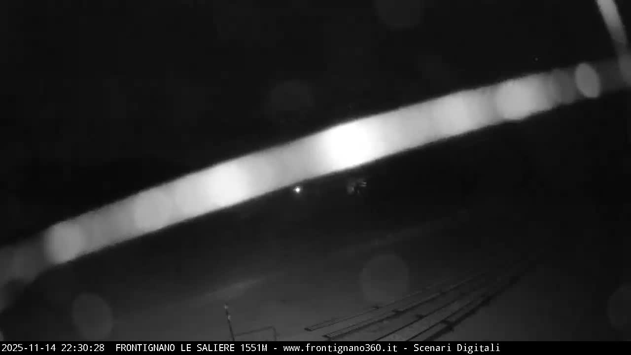 A very dark, blurry night view reveals a bright diagonal streak of light above faint railroad tracks, amidst scattered soft blurs suggesting a hazy or misty atmosphere.