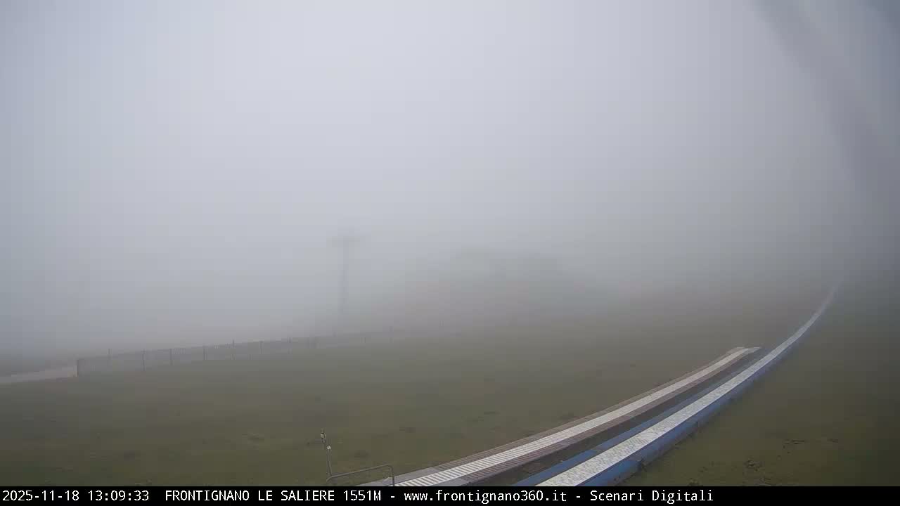 A very dark, blurry night view reveals a bright diagonal streak of light above faint railroad tracks, amidst scattered soft blurs suggesting a hazy or misty atmosphere.