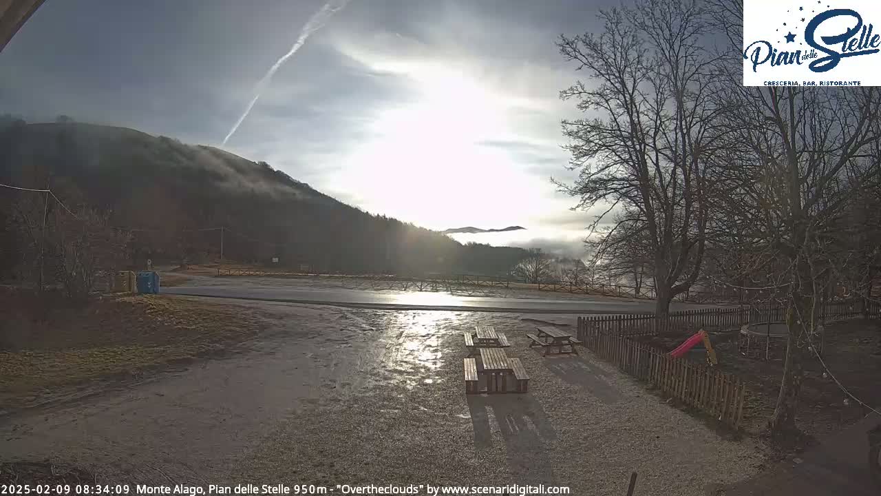 A mostly sunny day with fog in the valley shows a paved road leading to a mountain, with picnic tables and playground equipment in the foreground.
