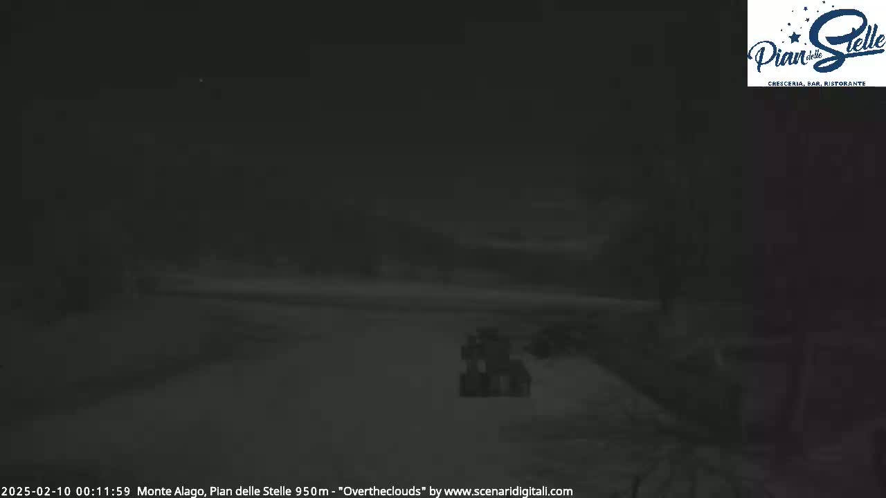 A dark, nighttime outdoor scene shows a mostly obscured, snow-covered area with a faint structure visible in the mid-ground.
