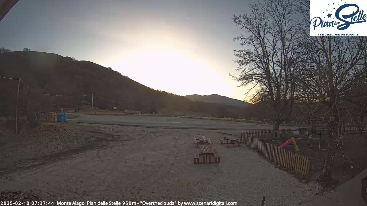 A sunrise illuminates a frosty, empty parking lot near a mountain, with picnic tables and a small playground visible in the foreground.