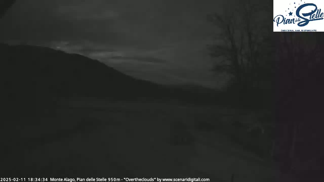A dark, overcast evening landscape shows a silhouetted mountain range and some trees under a cloudy sky.