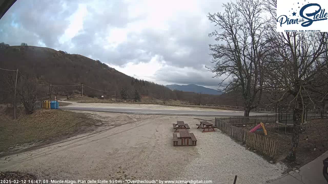 A gravel area with picnic tables is situated in front of a mountain under an overcast sky.