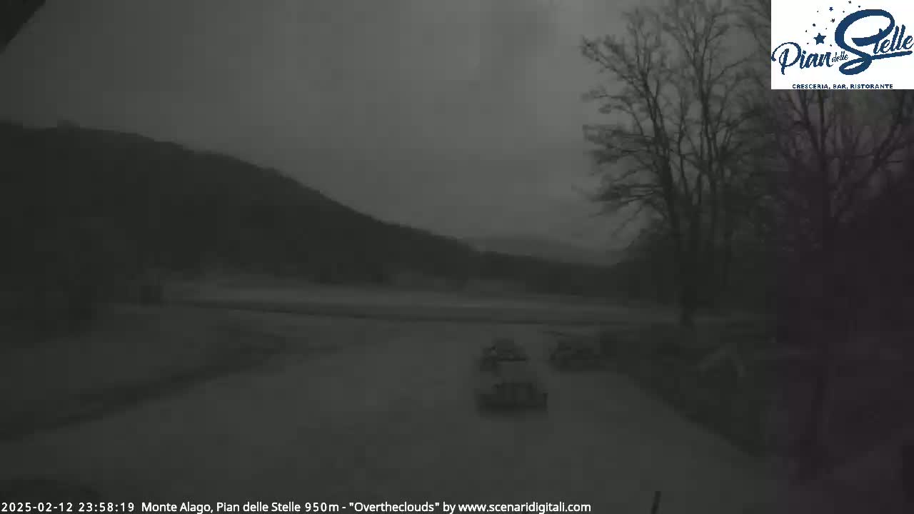 A dark, overcast scene shows a road with a few cars driving past trees and a hill in the distance.