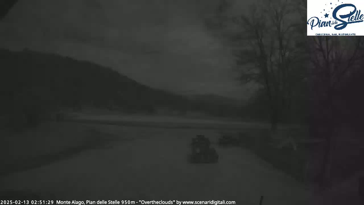 A dark, overcast scene shows two small vehicles traveling on a road, with mountains in the background and trees to the right.