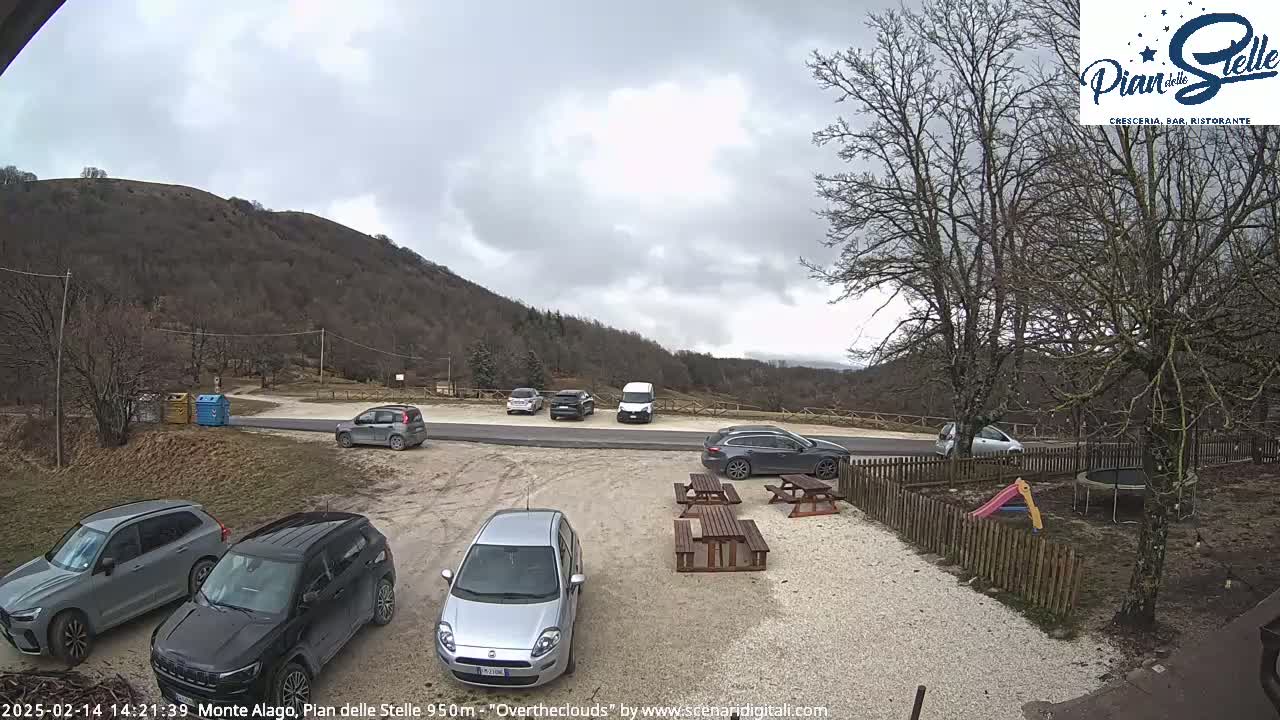 A parking lot with several cars is situated near a mountain under an overcast sky.