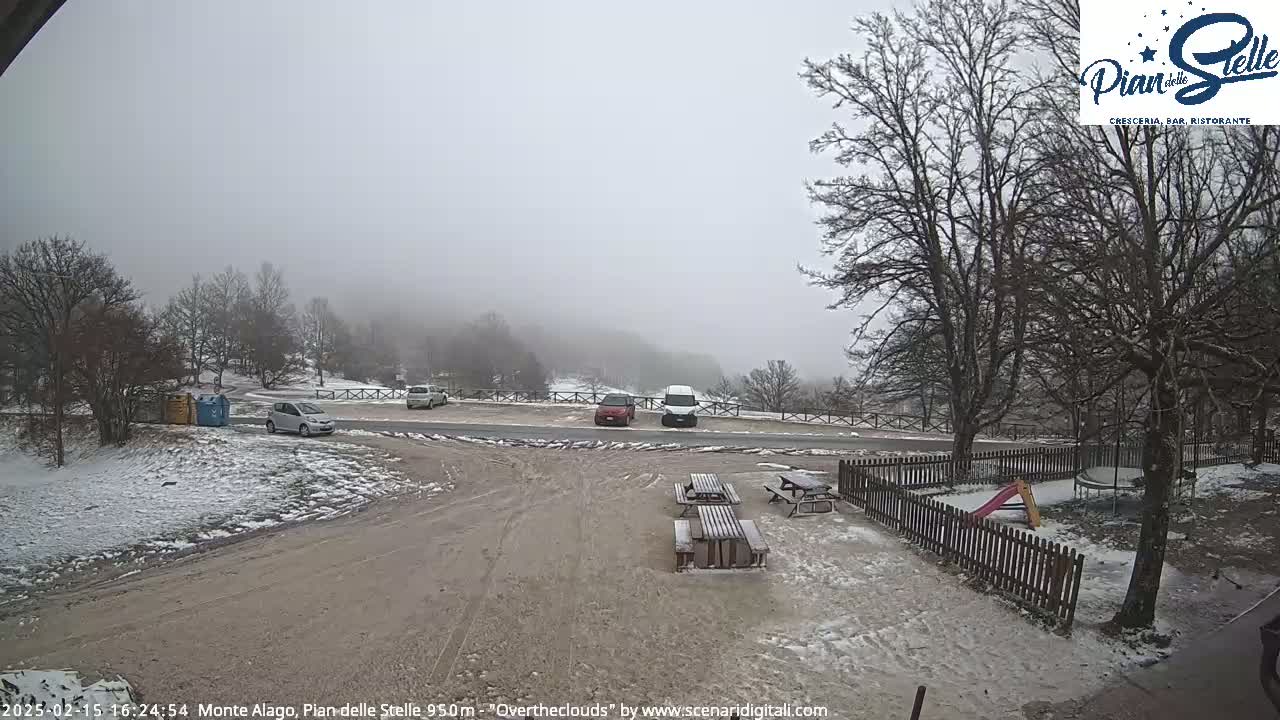A snowy parking lot with a few cars, picnic tables, and a playground is visible under an overcast sky.