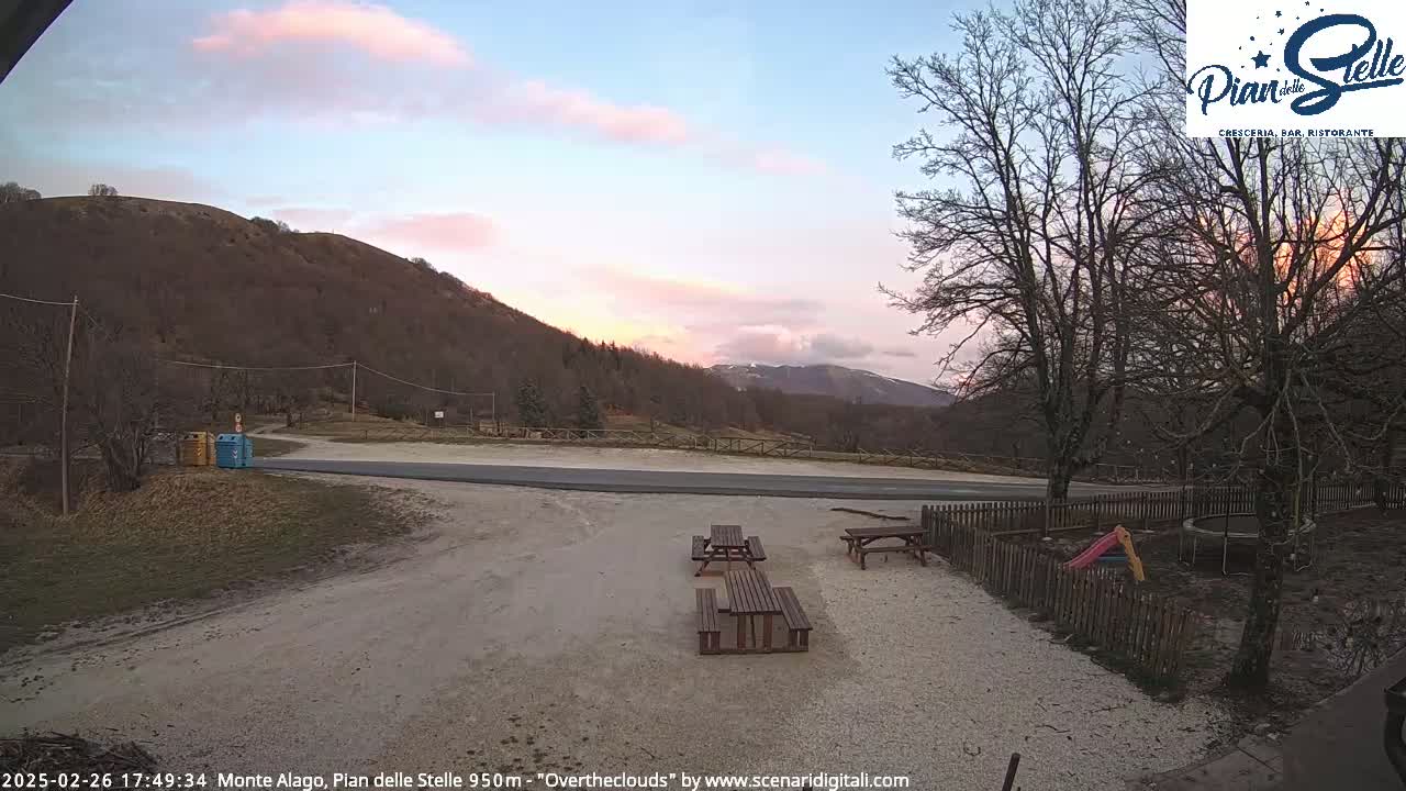 A mountainside parking area with picnic tables and playground equipment is visible under a pale pink sunset sky.
