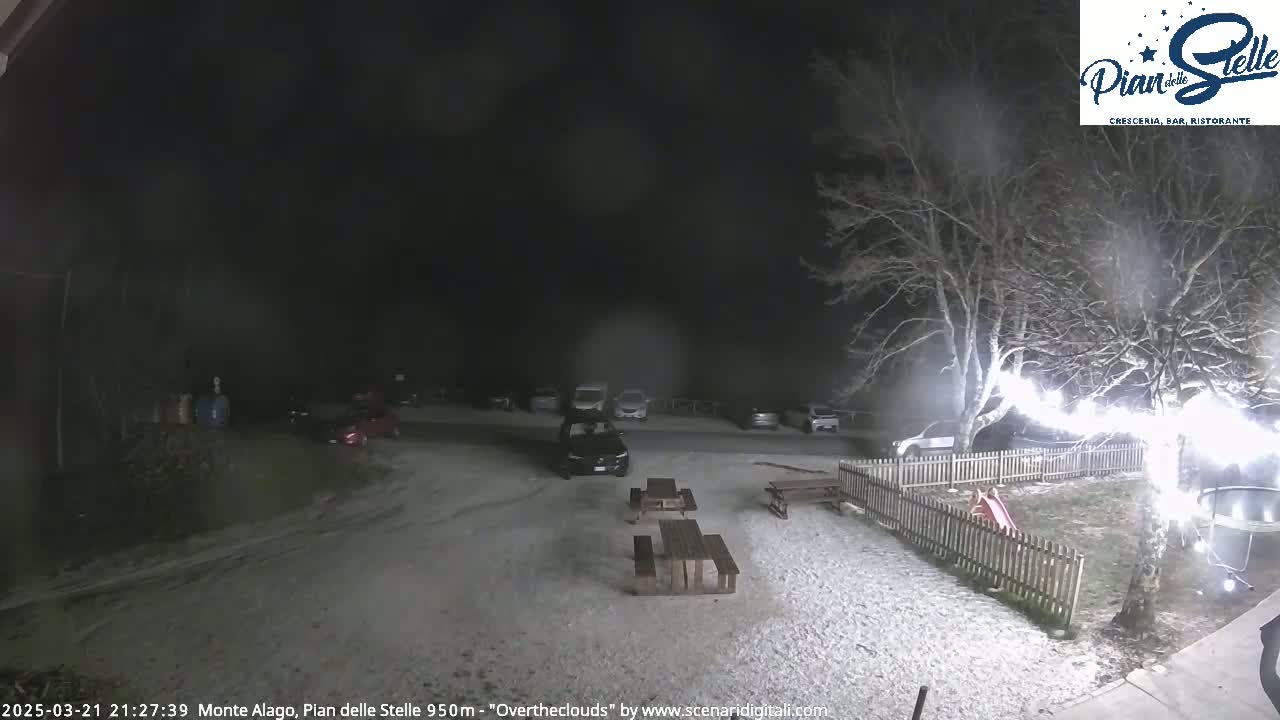 A snow-covered parking lot and outdoor seating area are visible at night, illuminated by artificial lights, with bare trees surrounding the scene.