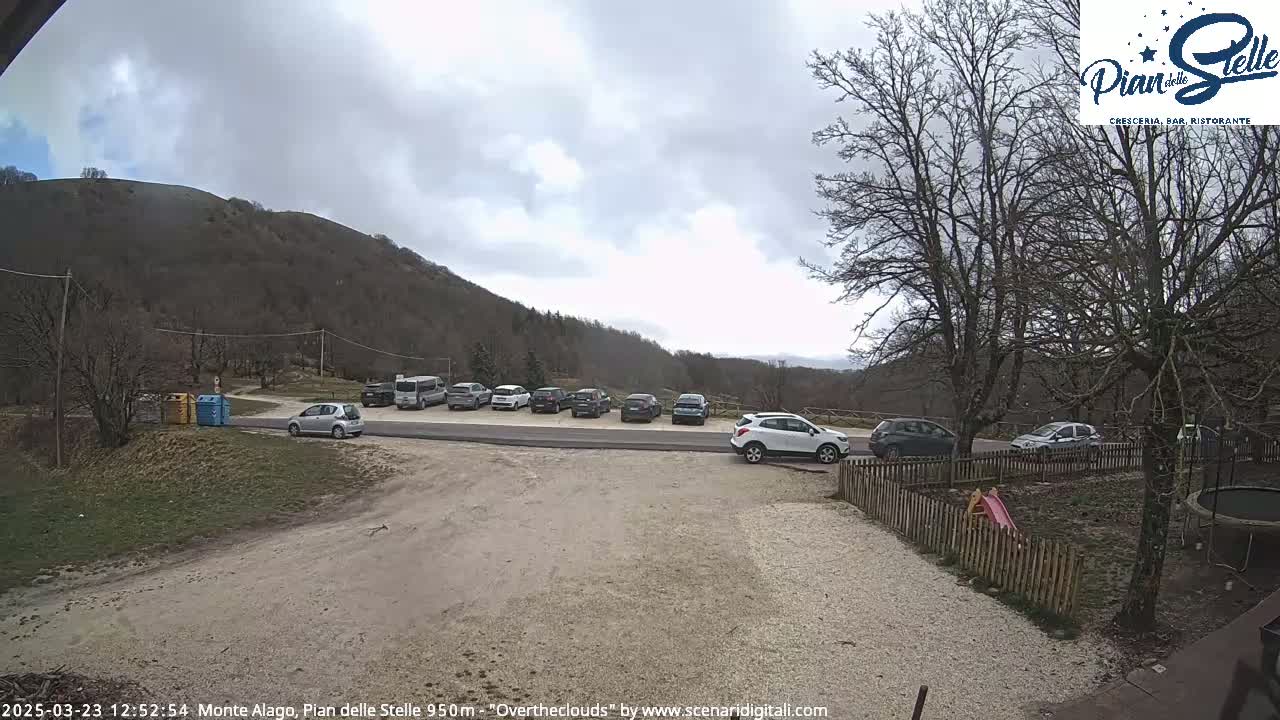 A parking lot with several cars is situated near a mountain under an overcast sky.