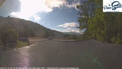 A mostly sunny day with scattered clouds is visible over a hilly landscape, partially obscured by a dark-colored shade structure in the foreground.