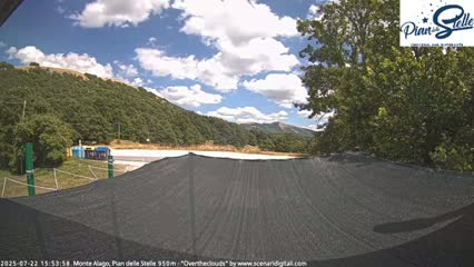 A mostly sunny day with scattered clouds is visible over a hilly landscape, partially obscured by a dark-colored shade structure in the foreground.