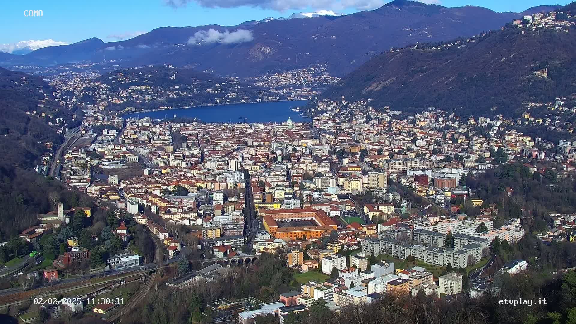 A sprawling city nestled in a valley between mountains, under a mostly clear blue sky.