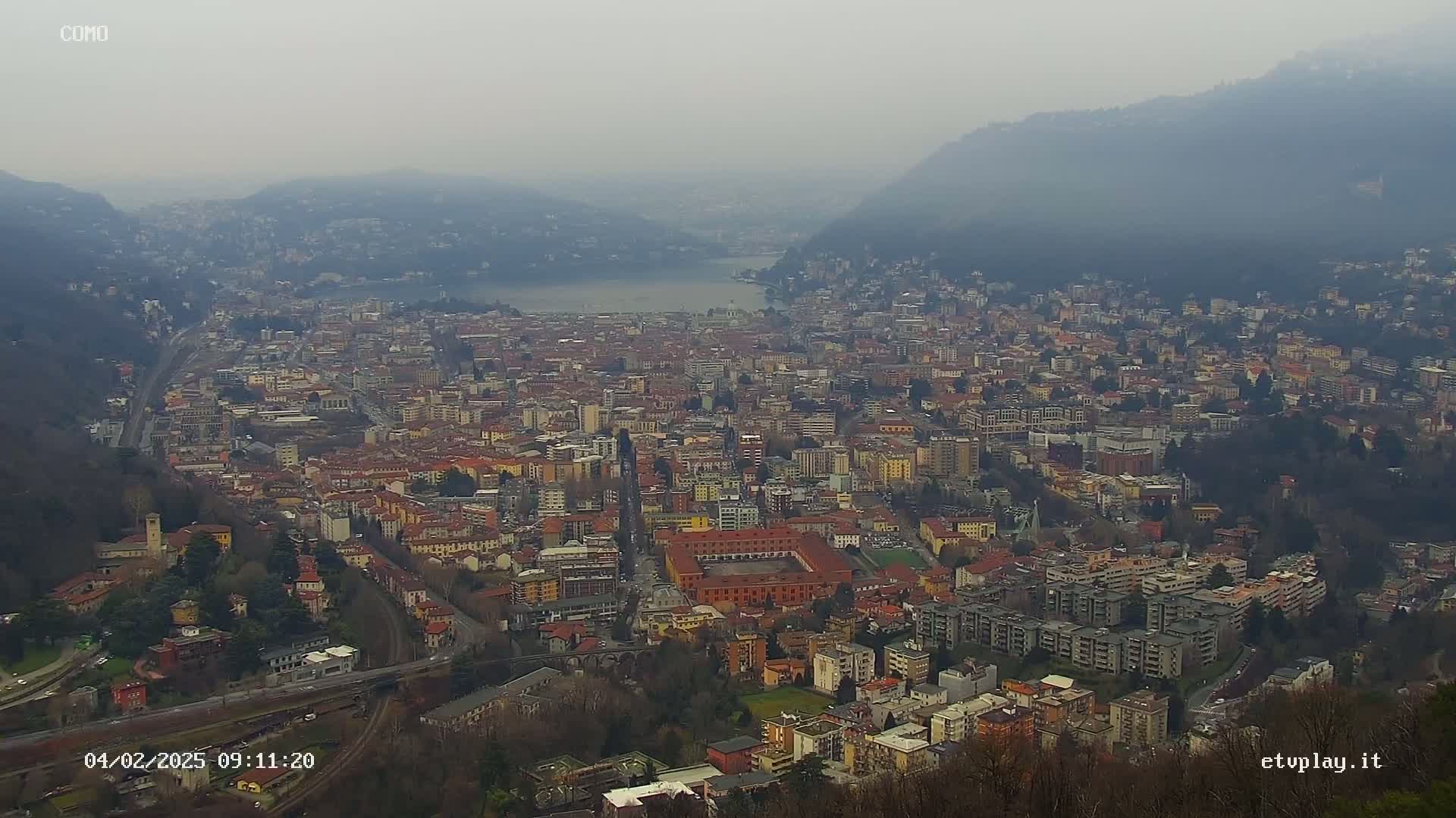 A hazy, high-angle view of a city nestled between hills and a body of water.