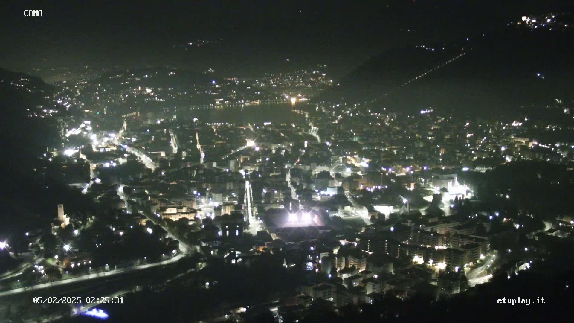 A nighttime, high-angle view of a city illuminated by streetlights and building lights, situated near a body of water.