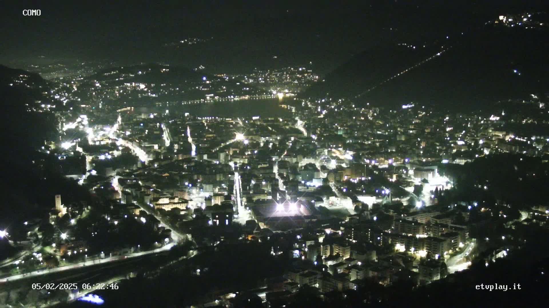 A nighttime, high-angle view of a city nestled in a valley, illuminated by numerous streetlights and building lights.