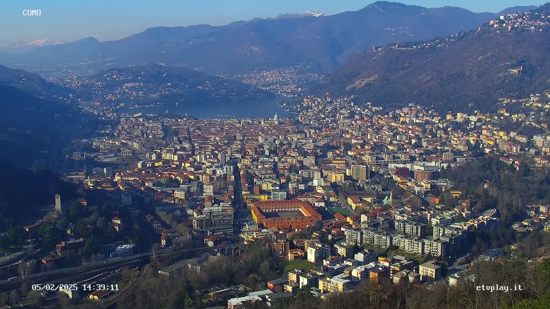 A sprawling city nestled in a valley between mountains, under a clear sunny sky.