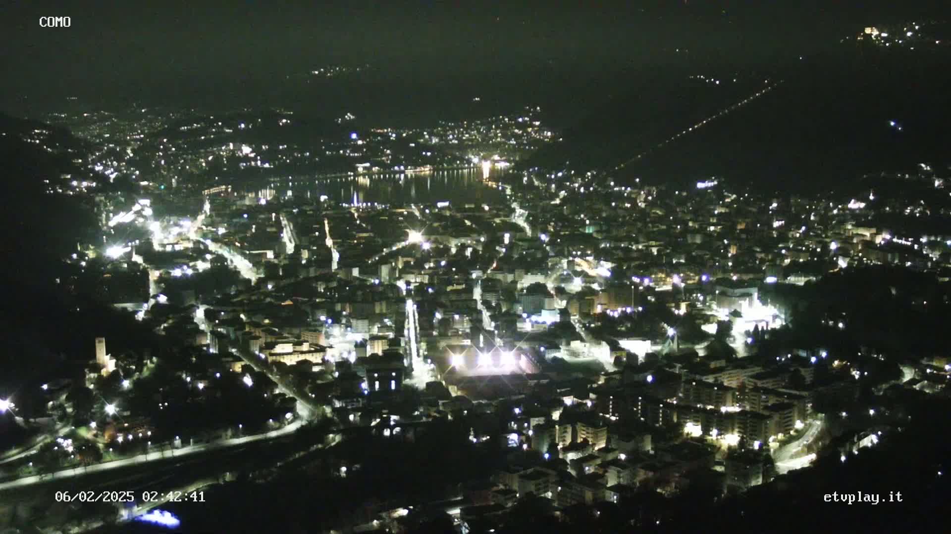 A nighttime, high-angle view of a city illuminated by lights, situated near a body of water.