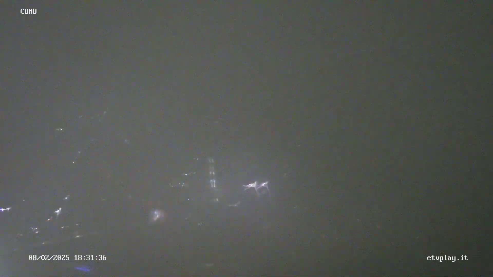 A low-light, possibly nighttime, image shows faint, scattered light sources against a dark, hazy sky.