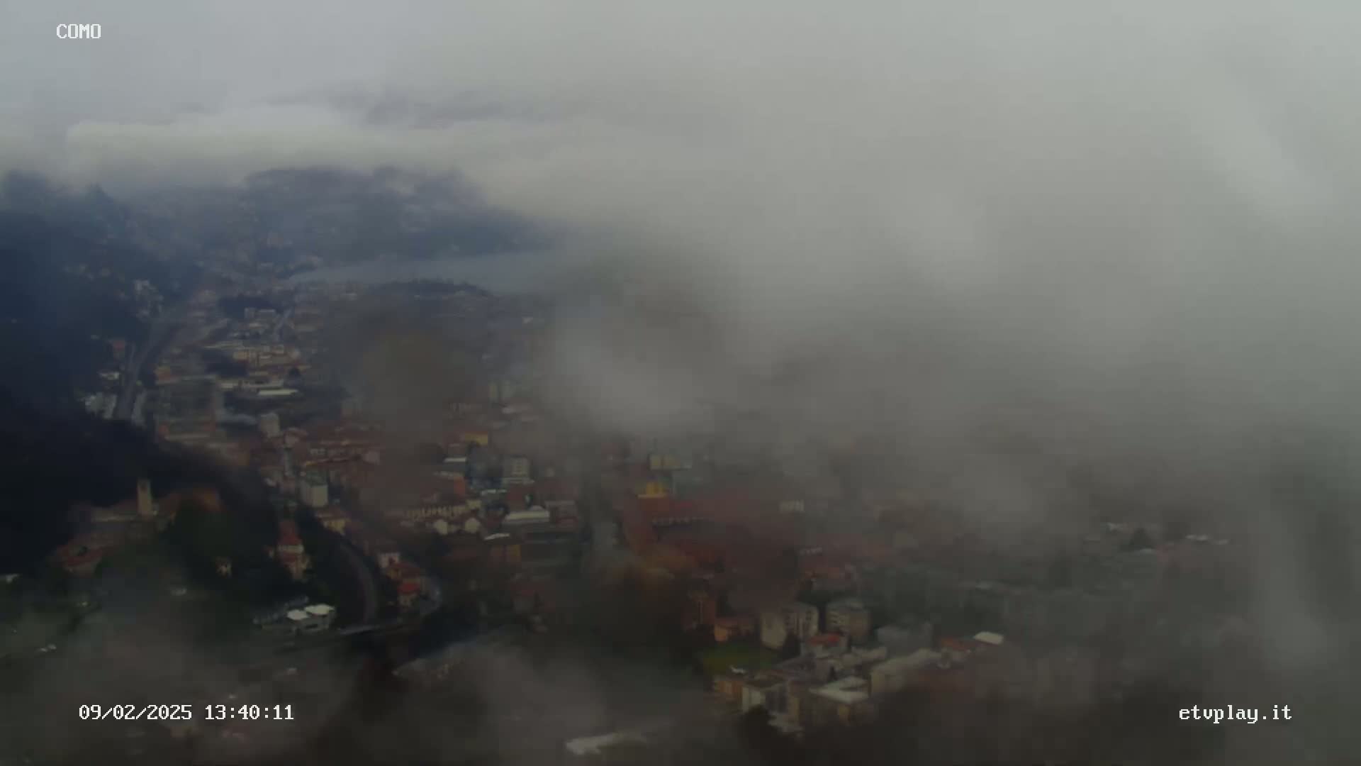 A foggy view overlooks a city nestled in a valley, partially obscured by low-hanging clouds.