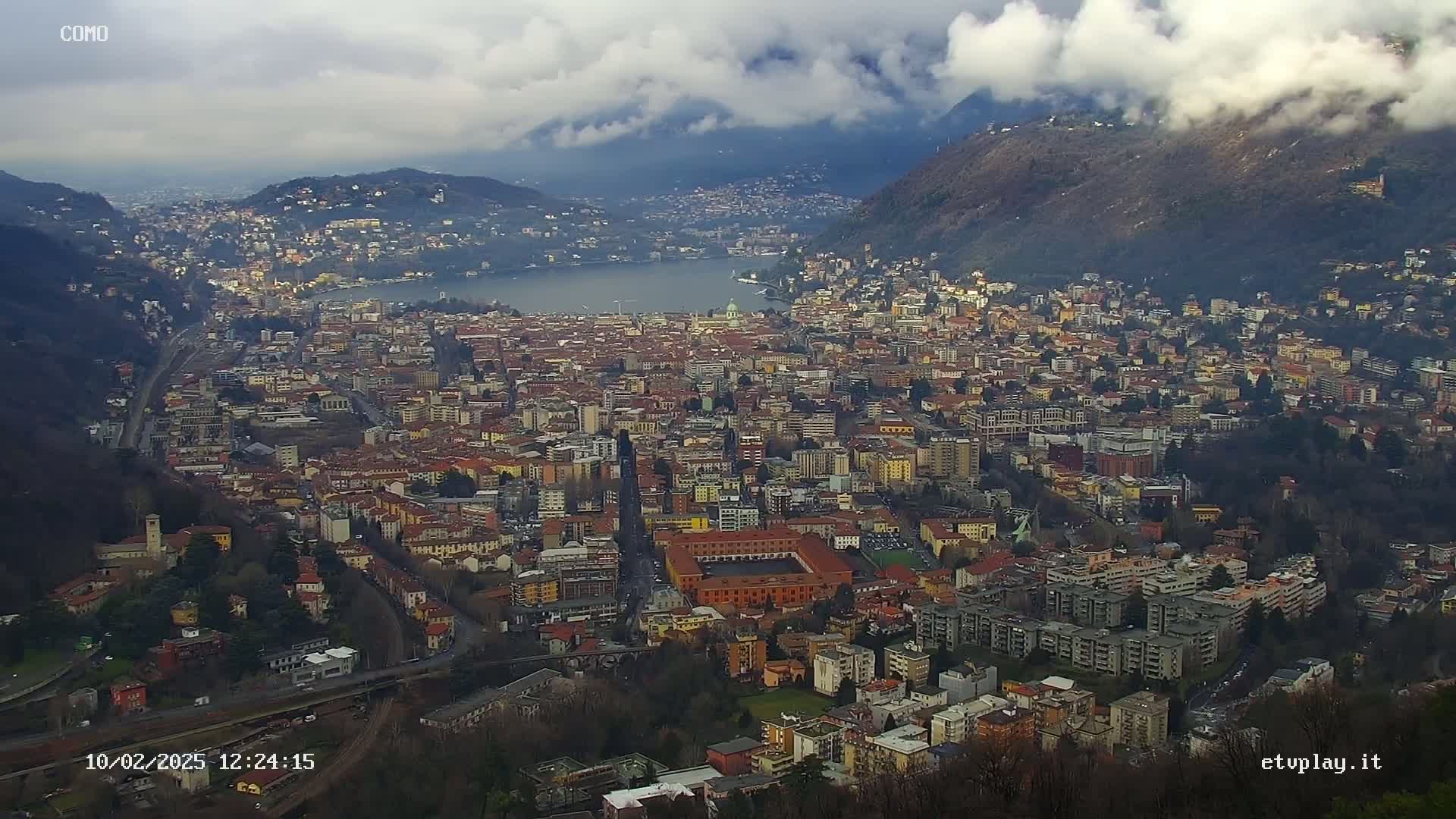 A sprawling city nestled between mountains and a lake under a cloudy sky.