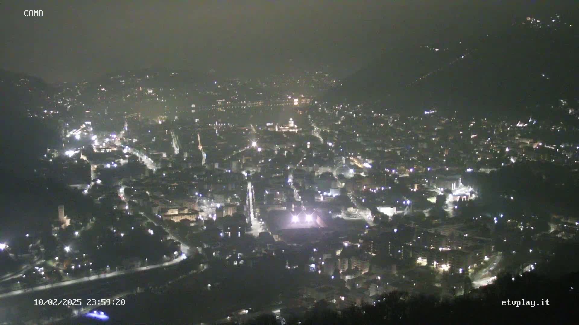 A nighttime aerial view of a city nestled in a valley, shrouded in a hazy atmosphere.