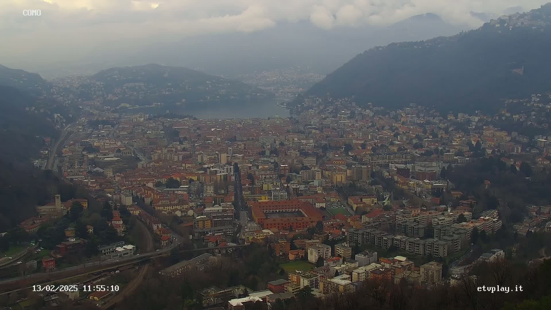 A sprawling city nestled between mountains, overlooking a lake under an overcast sky.
