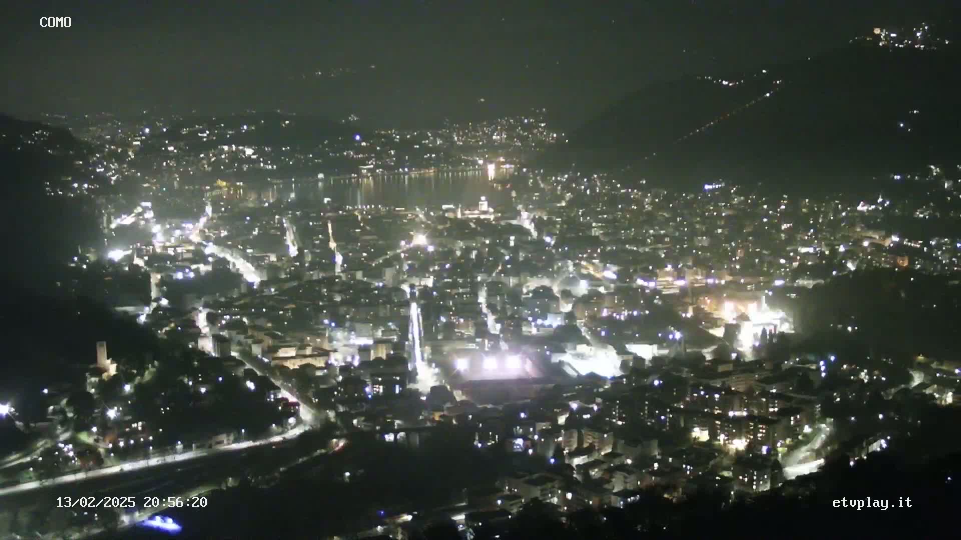 A nighttime, high-angle view of a city illuminated by lights, situated beside a body of water under a clear sky.