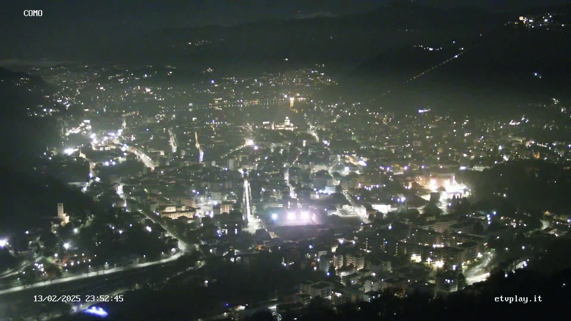 A nighttime, high-angle view of a city illuminated by streetlights and building lights, nestled in a valley.