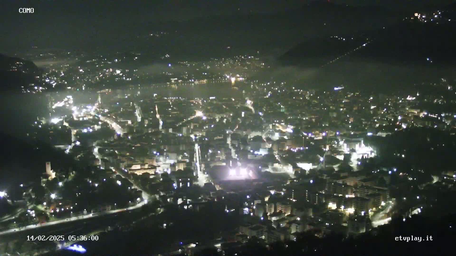 A nighttime aerial view of a city partially shrouded in fog, showing numerous illuminated buildings and roads.