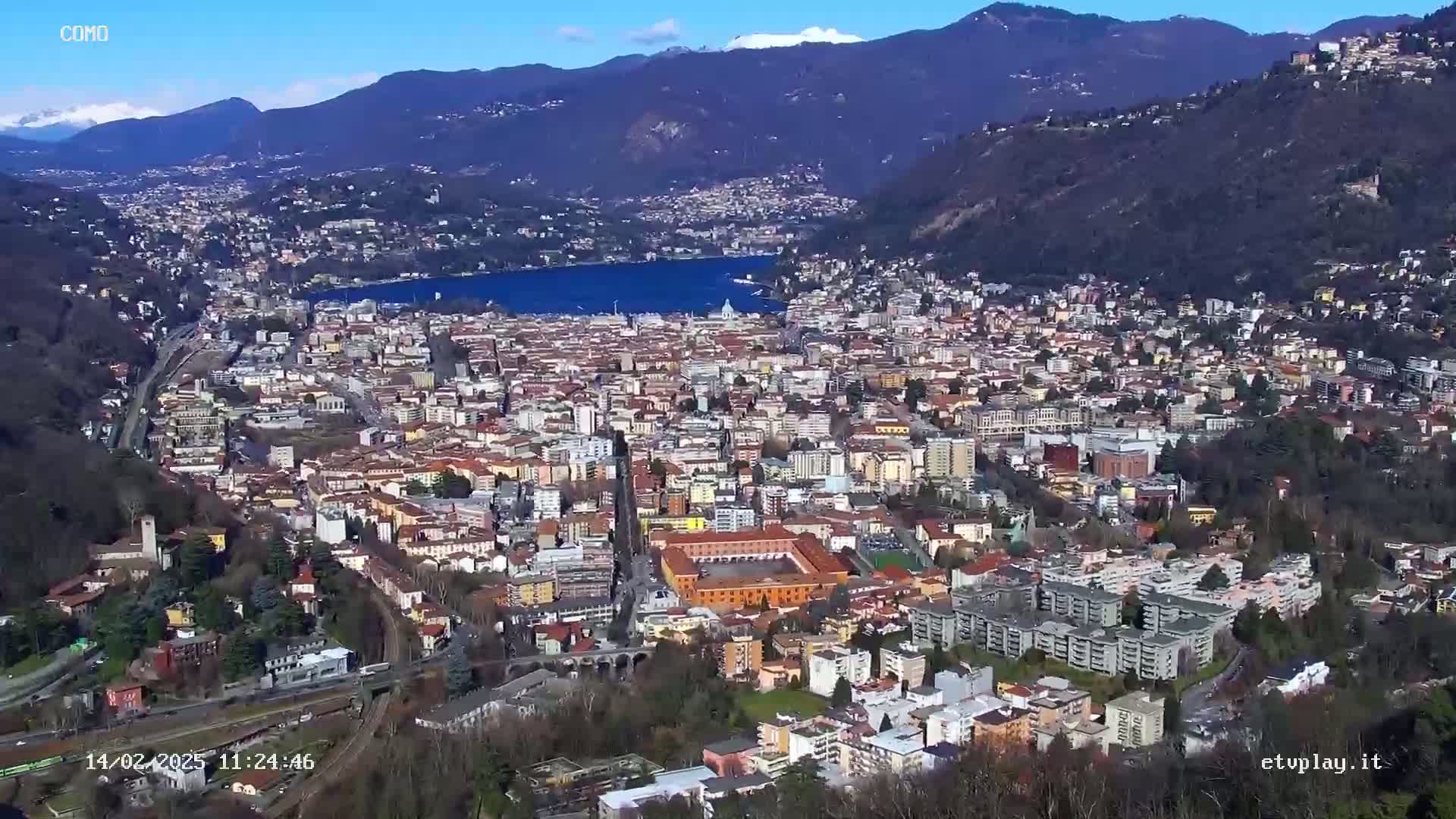 A sprawling city nestled in a valley between mountains, overlooking a lake under a clear, sunny sky.